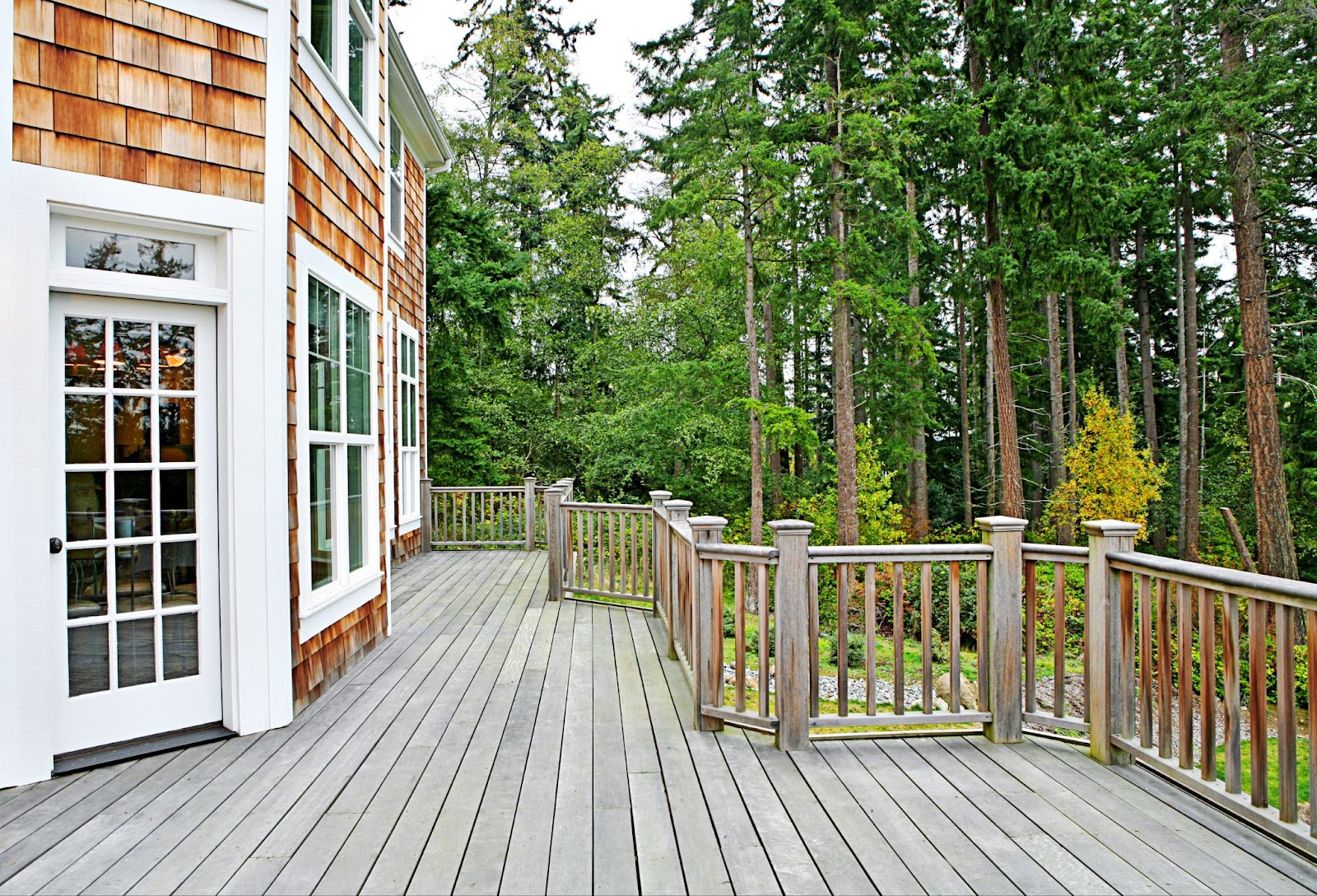 Large wooden deck attached to a wooden house with white framing.