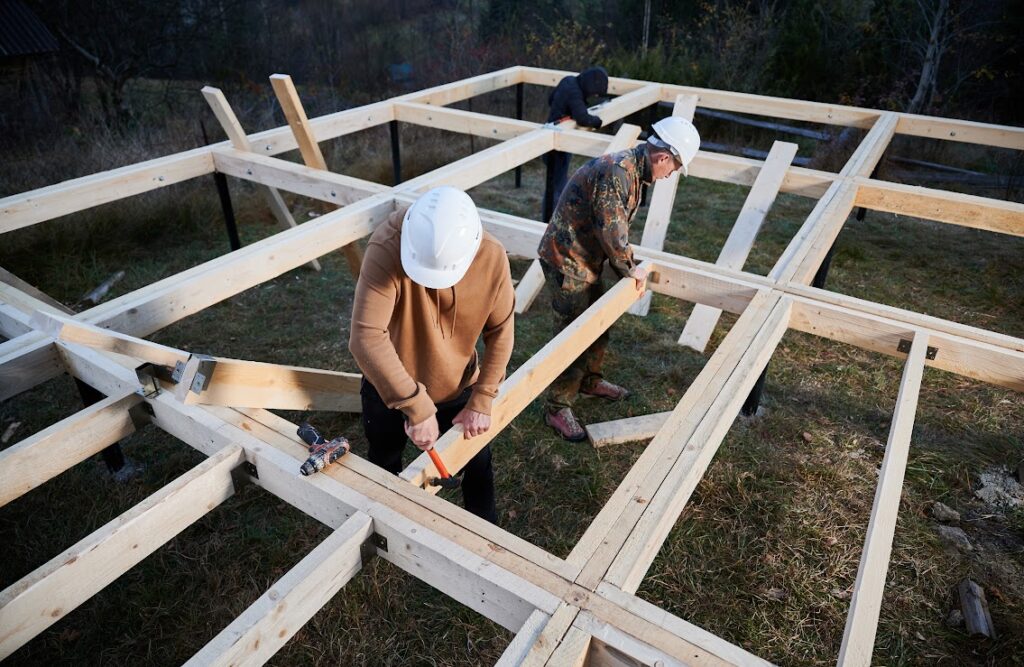 Two men wearing white hardhats laying planks of wood down for a deck.