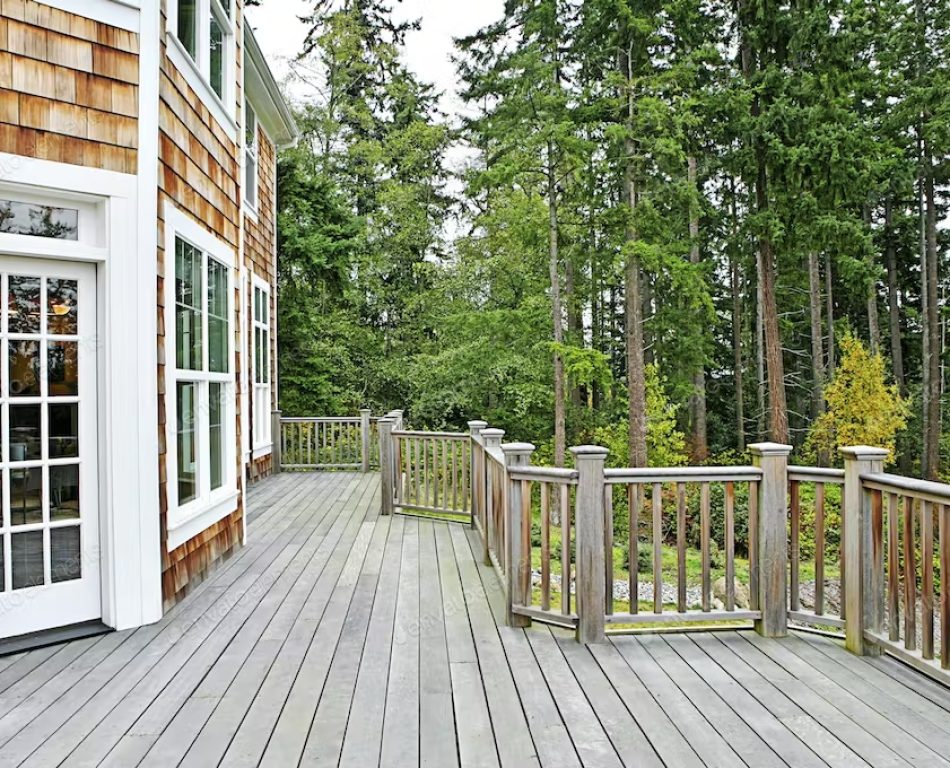 Large wooden deck attached to a wooden house with white framing.