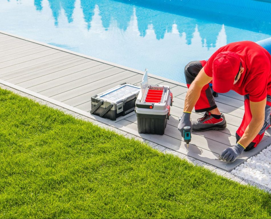 A man with a red shirt and ball cap installing composite decking next to a pool.