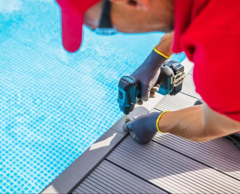 A man in a red shirt installing composite decking near a swimming pool.